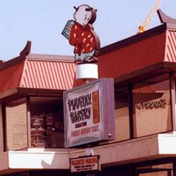 A close-up view of a bakery sign that stands in front of a two-story building.