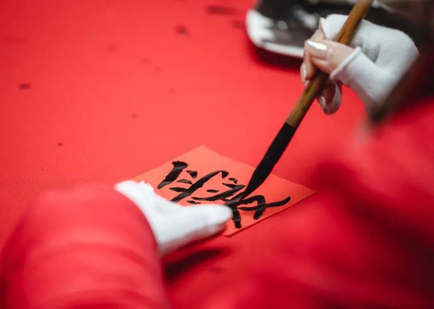 A person paints Chinese characters on red paper with a long wooden brush.