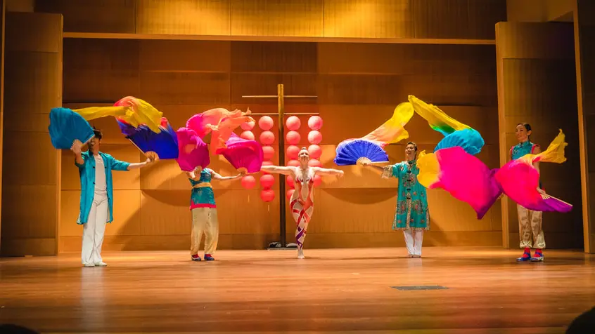 A group of dancers on stage raise colorful fabrics in the air.