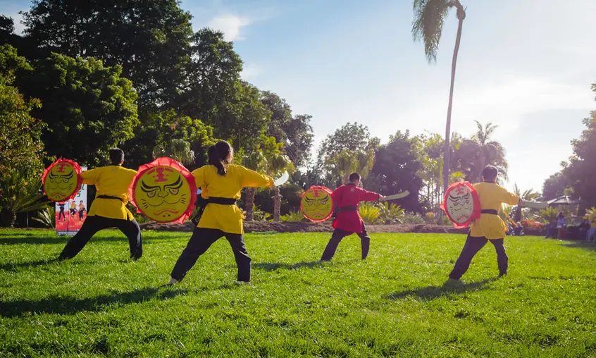 A group of drummers in yellow outfits perform outdoors on a green lawn.