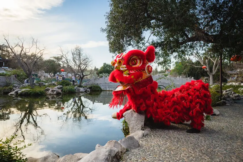 A red dragon puppet sits near a lake.