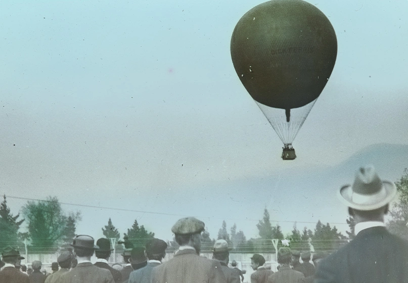 A crowd watches a hot air balloon in the sky.