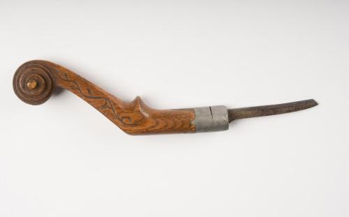 Crooked knife with metal blade attached to wooden handle with spiral relief and carved vine motif at the handle top.