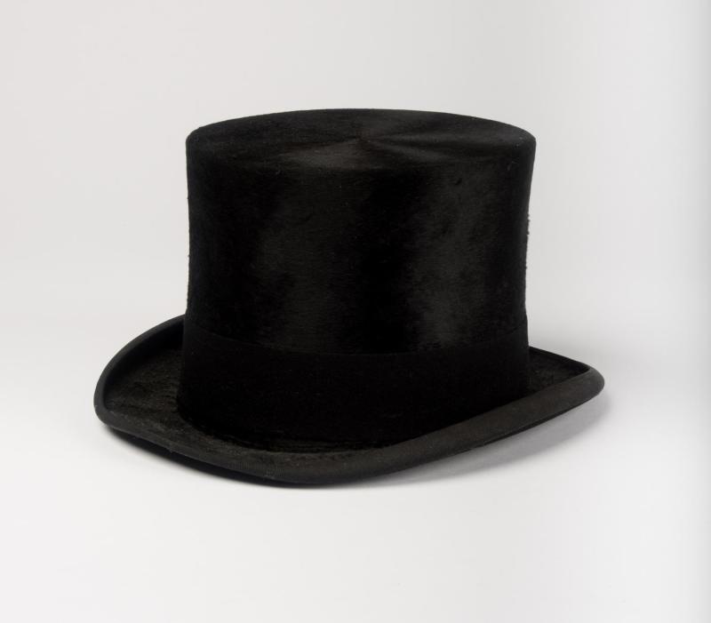 Black beaver-skin top hat sitting on plain surface against a plain, white background.