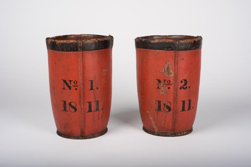 Rear view of two red, leather bucket. The back of one reads "No. 1, 1811". The other reads "No. 2, 1811."