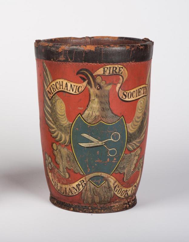 Red leather bucket decorated with an eagle bearing a blue shield with scissors. A Banner in its beak reads "Mechanic Fire Society"; banner in its talons reads "William P. Gookin."