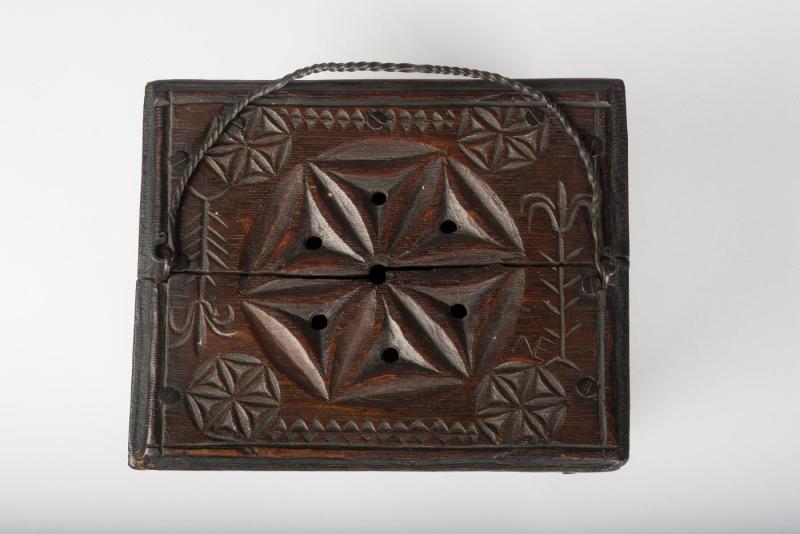 Overhead view of brown wooden box foot-warmer with perforated star-shaped designs carved into it and a thin iron handle.