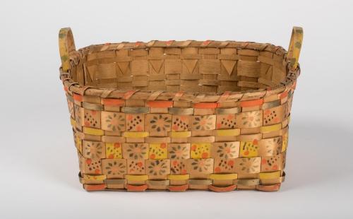 Oval-shaped splint woven basket with handles, stamped with flowers and dots with additional yellow, orange and green patterns interwoven on some splints.