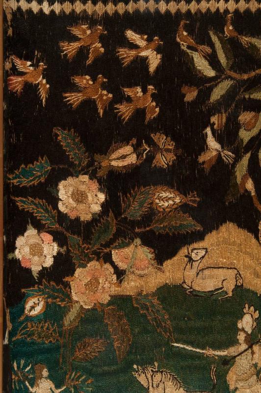 Detail of embroidery featuring birds, foliage, ox, figures, and horses set against dark background.