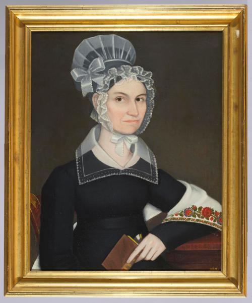 Portrait of a seated white woman dressed in black, holding a book, and wearing a colorful shawl over the crook of her left arm, all set against a plain dark background. 