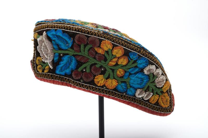 Black velvet cap in the shape of a pointed oval, with beadwork in blue, white, green, yellow, and red forming flowers and stems all over; made by a Haudenosaunee woman. 