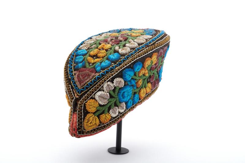 Black velvet cap in the shape of a pointed oval, with beadwork in blue, white, green, yellow, and red forming flowers and stems all over; made by a Haudenosaunee woman. 