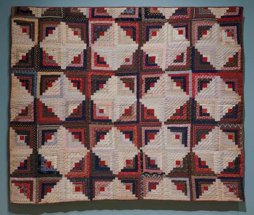 Quilt with overall checkerboard pattern, alternating between cream and red-toned squares; each square consists of many skinny strips of varying colors. 