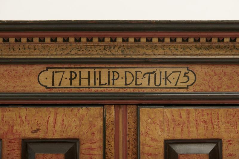 Close-up view of the top of a large wooden wardrobe with an inscription that reads "17 Philip Detuk 75." 