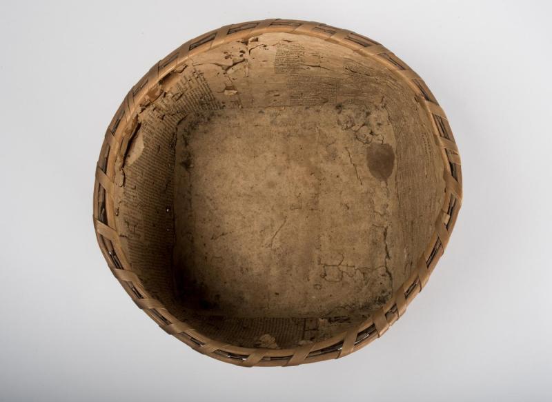 Interior of a woven brown basket made from strips of ash wood and lined with newspaper. 