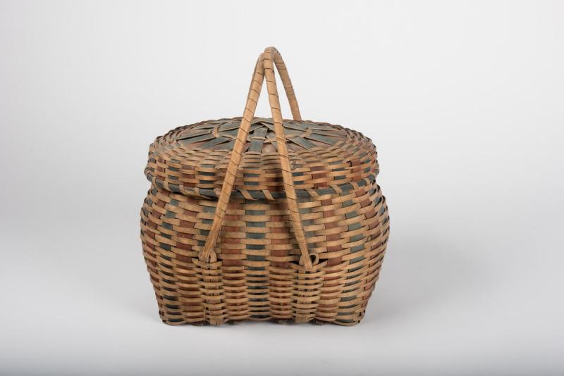 Oval-shaped woven basket with lid and movable handles, with indigo and red splints interwoven throughout.