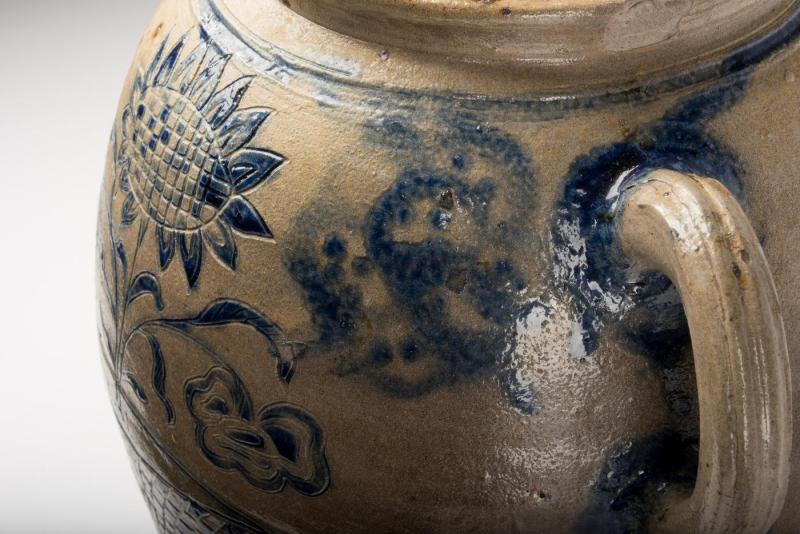 Close-up detail of handle and decoration on stoneware jar in blue pigment of a flower in a checkered pot.