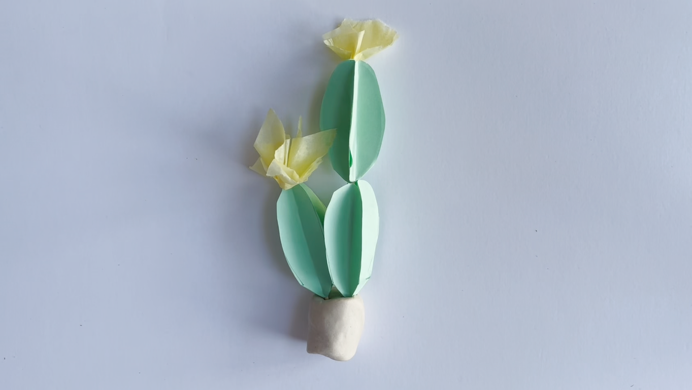 A small green paper version of a prickly pear cactus is adorned with yellow paper flowers.