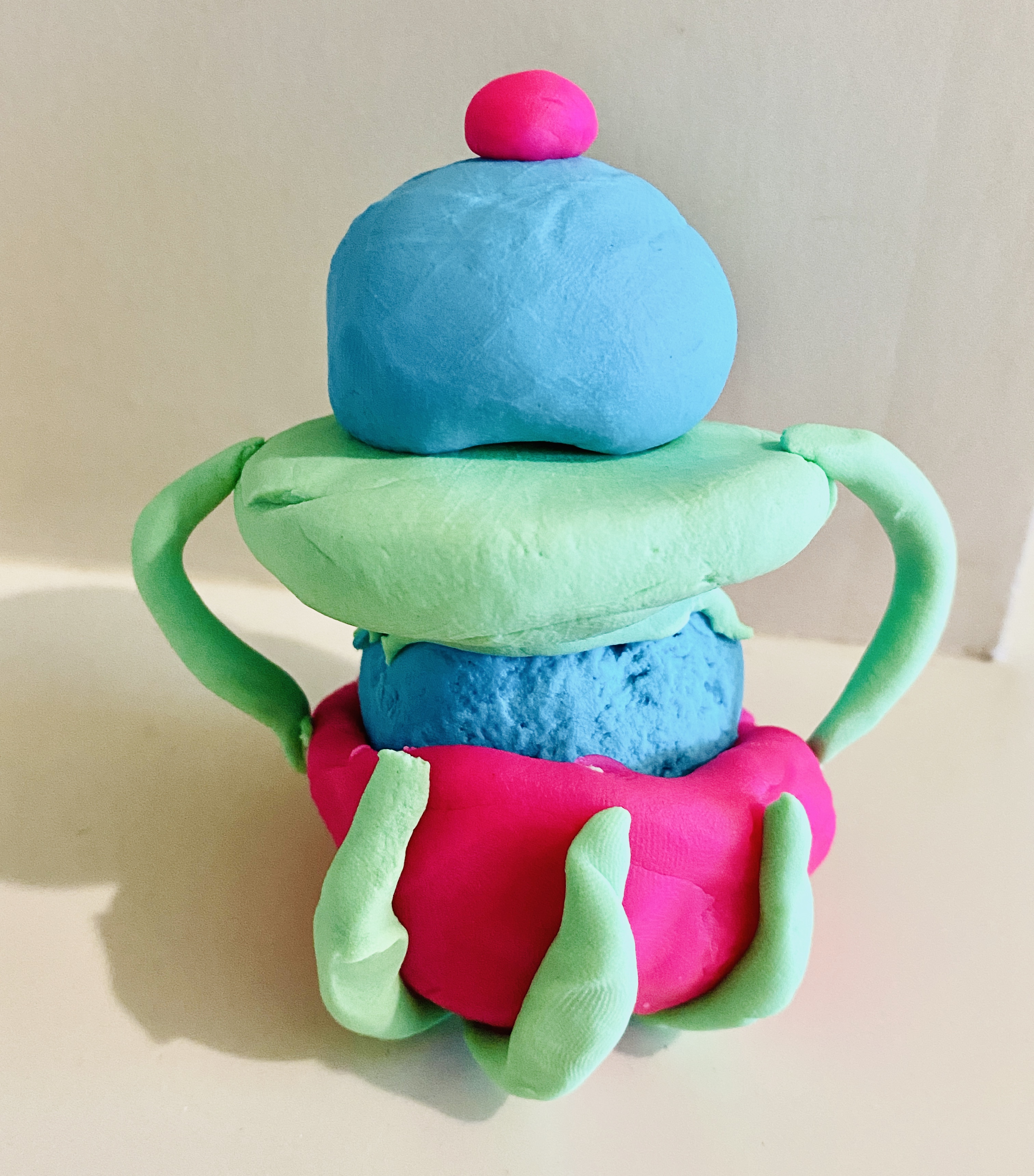 Blue, green, and pink clay stacked pot with green handles, a blue lid and a pink dot on the top. 