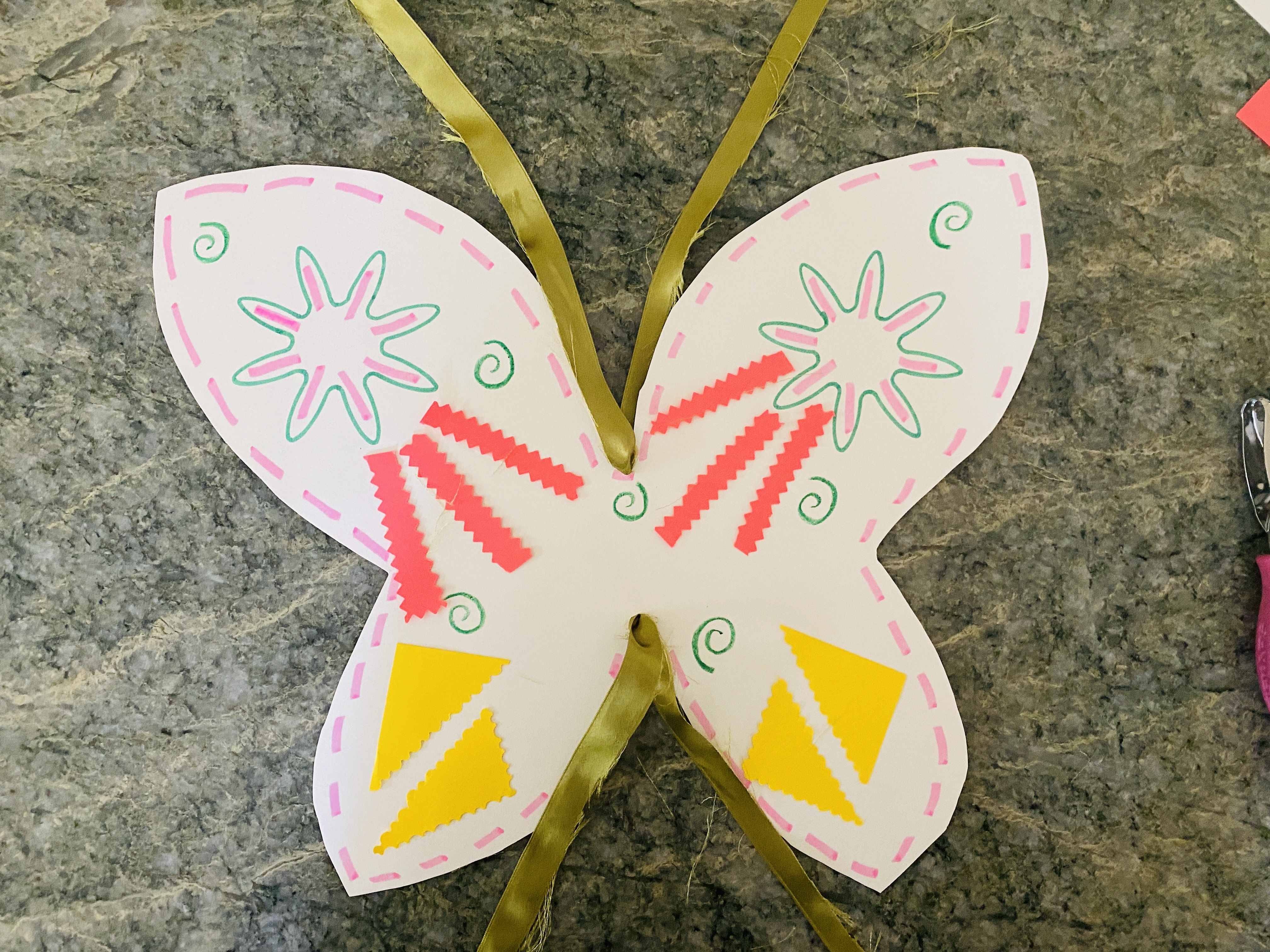 Hand-cut and decorated fairy wings with yellow and pink decorations and green ribbon attached on the top.