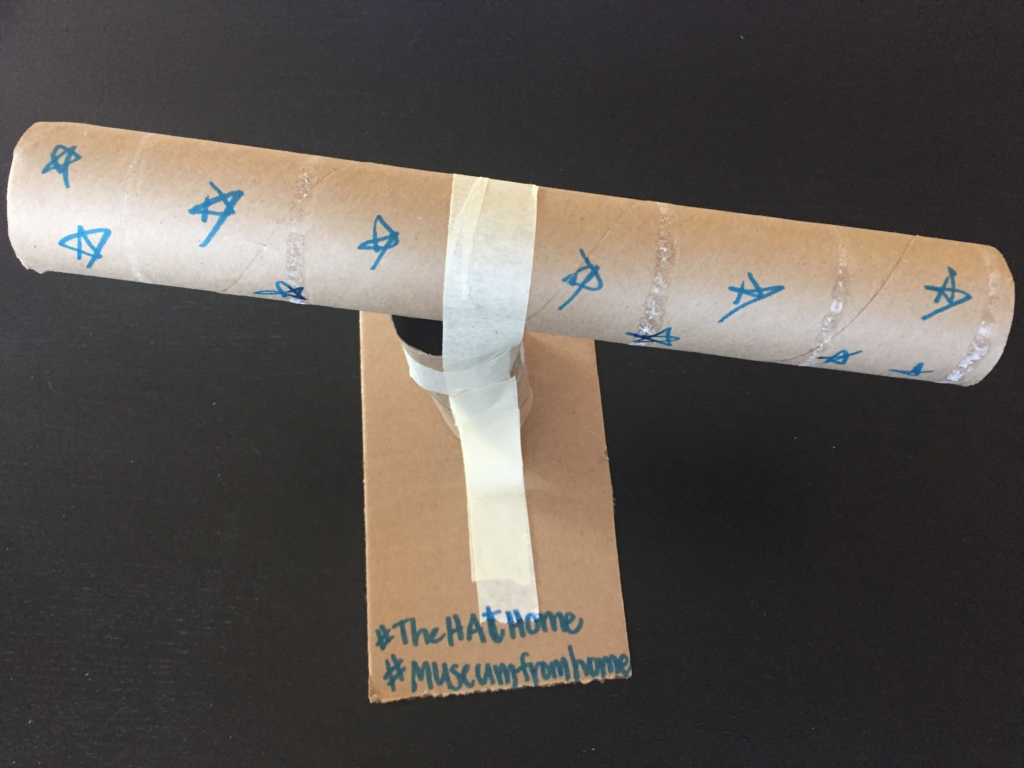 Brown paper towel roll decorated with blue stars taped to a smaller brown roll and a small brown piece of rectangle to create a homemade telescope.