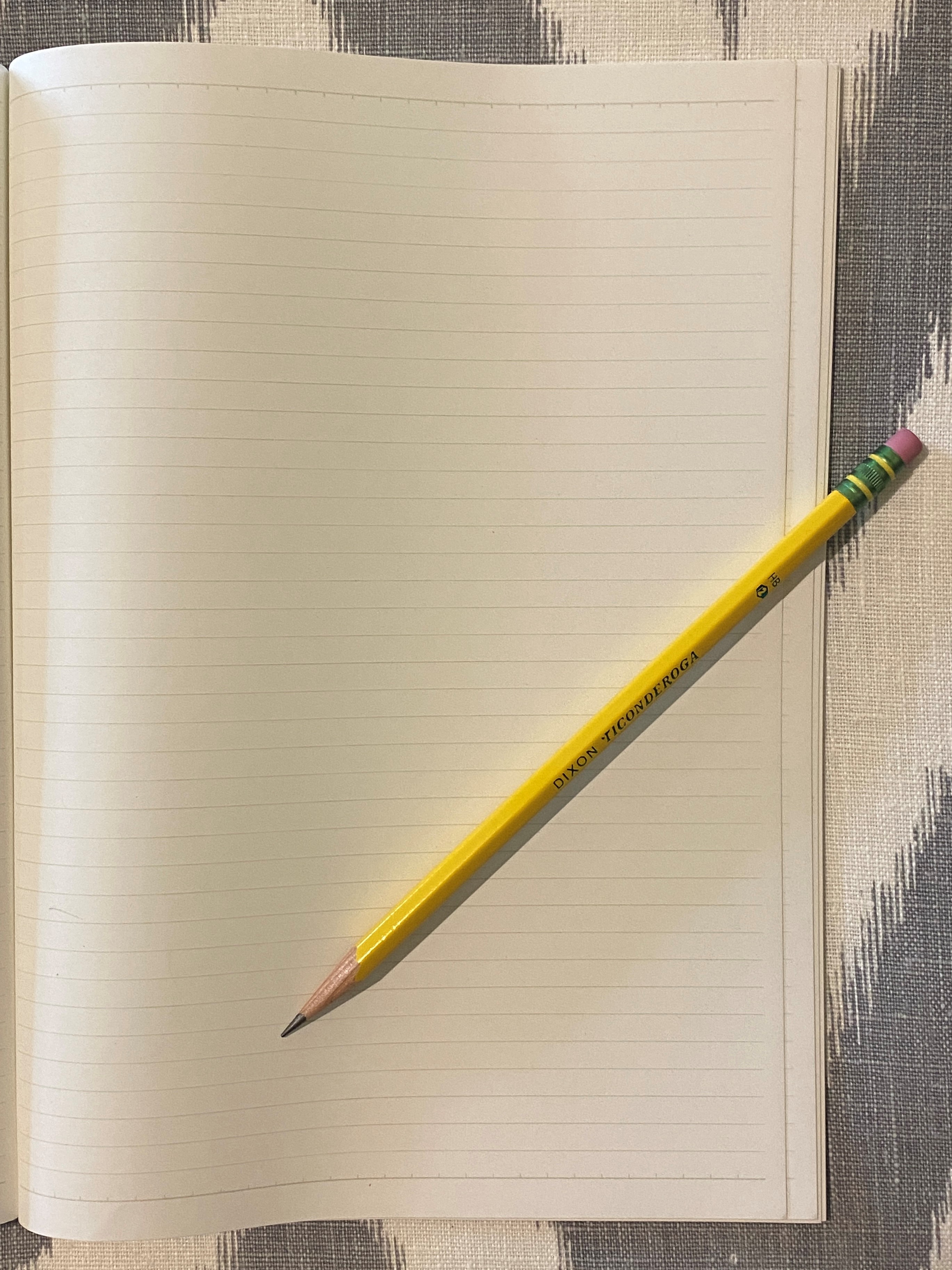 Lined notebook with a yellow pencil against a gray and white background.