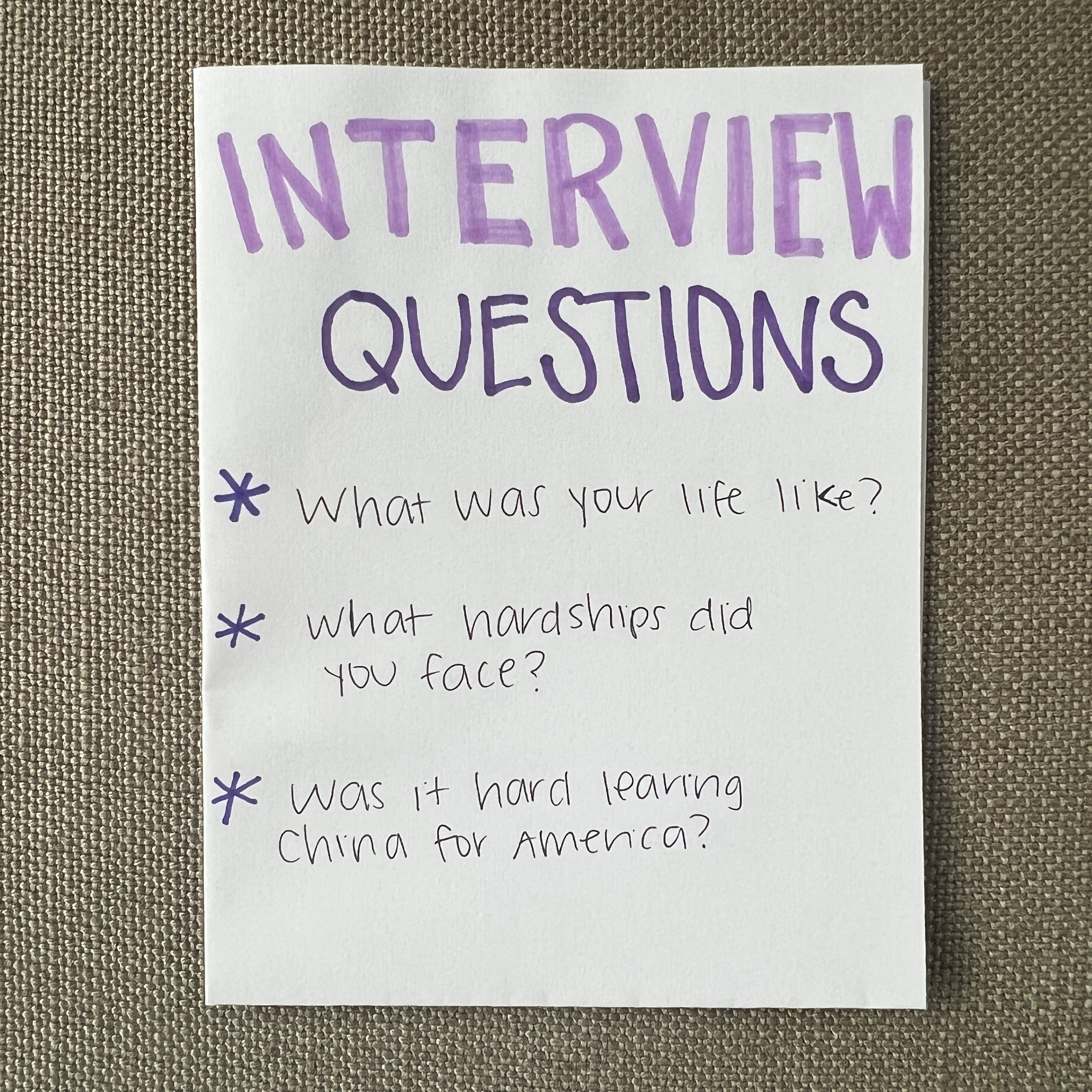 White piece of paper with purple writing that says "Interview Questions" at the top and three questions written below.