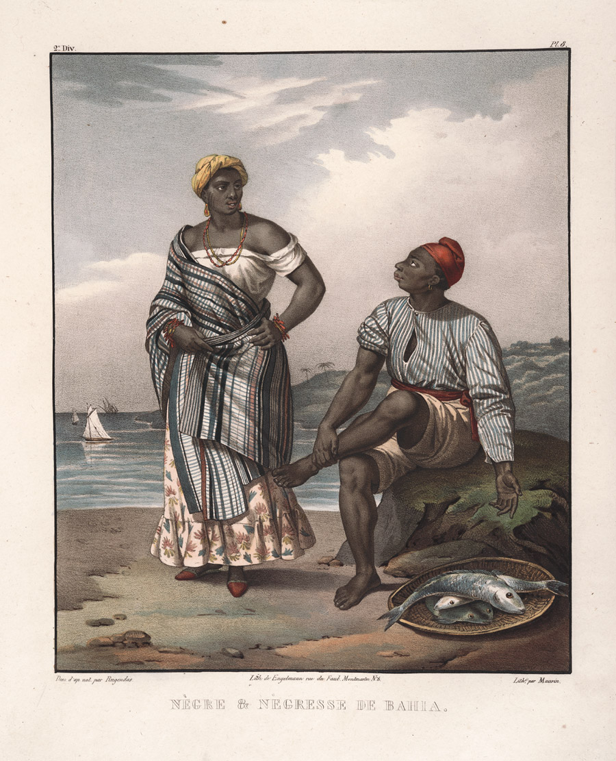 A man sits on a rock on a beach and looks up at a woman.