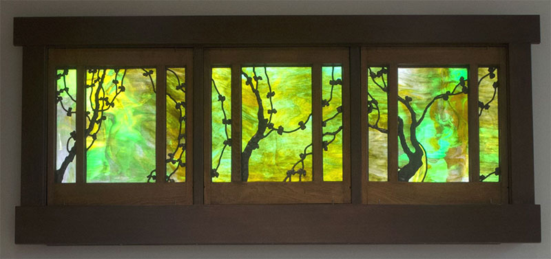 A 3 piece art glass panel with green hues, enveloped in a dark wood frame.