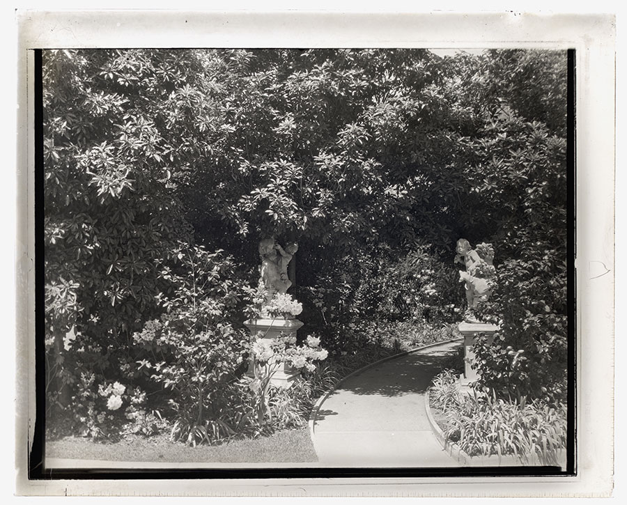 Black-and-white photo of a garden pathway with two statues.