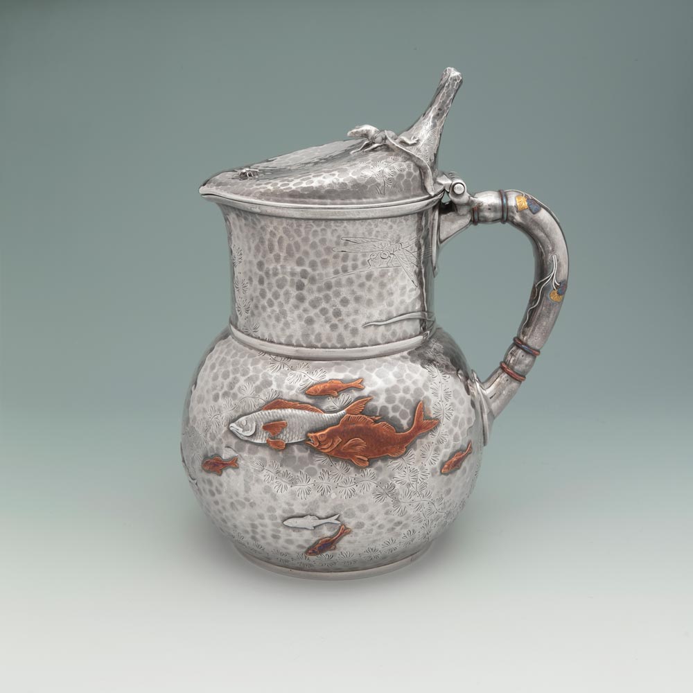 A small silver pitcher with swimming fish around the base.