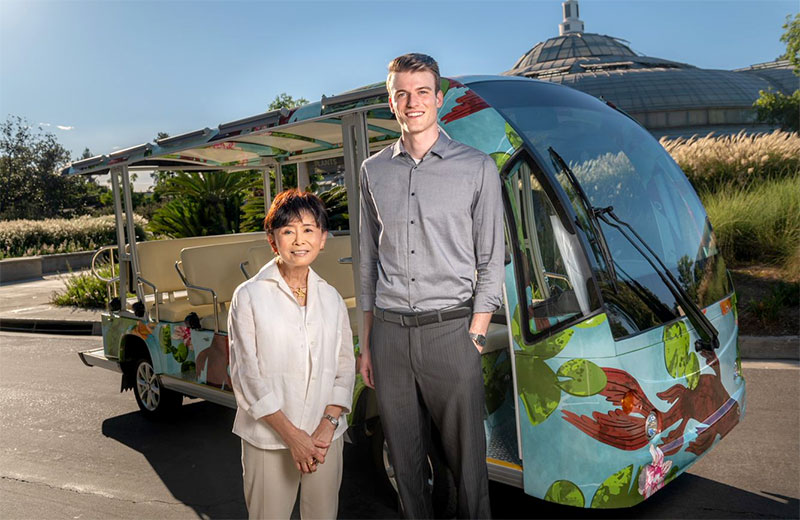 Two people stand in front of an electric passenger vehicle that's wrapped in a koi-inspired design.