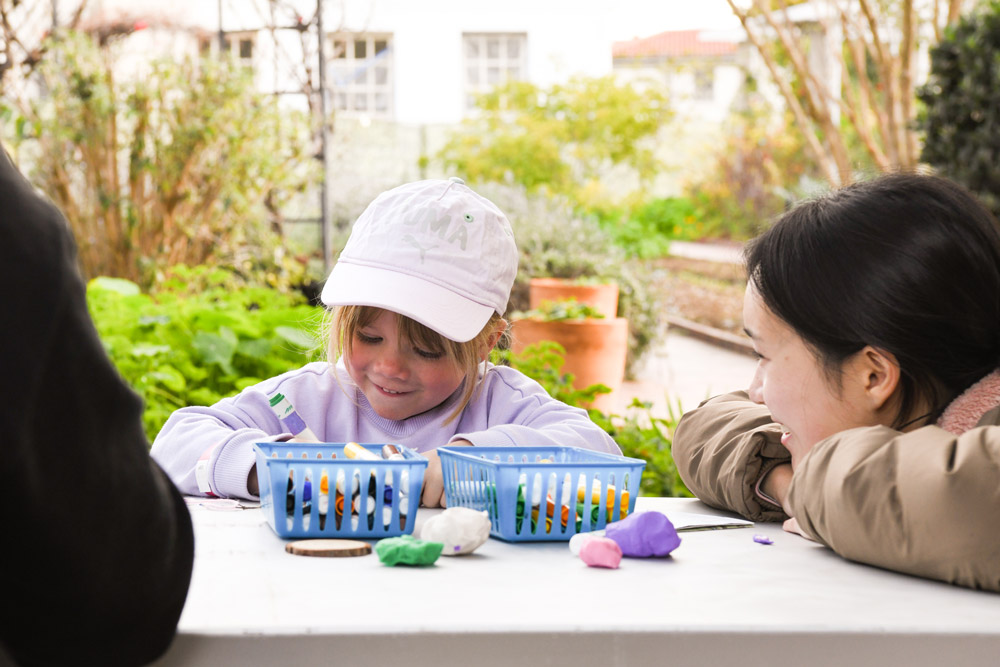 A child sits at a table with art supplies as an adult looks on.