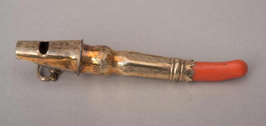 A small brass teething stick with a coral nub at one end and a whistle on the other end.