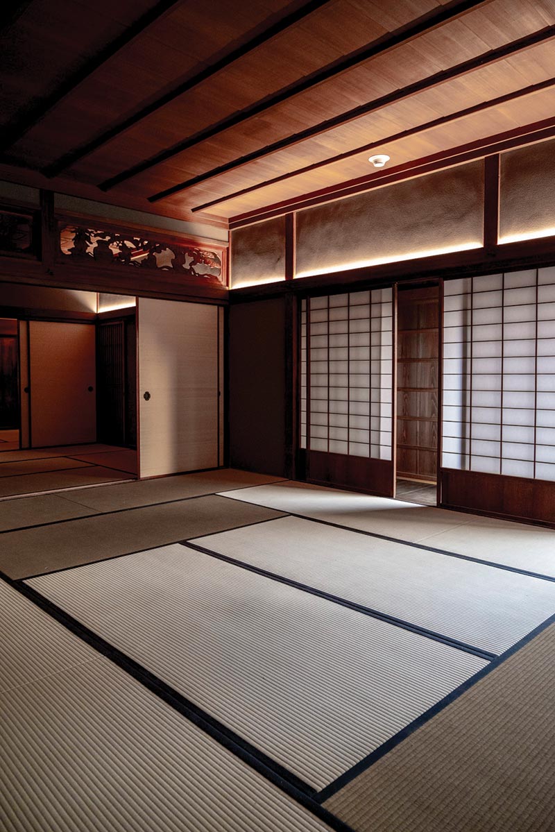 Sunlight seeps through a partially-open Japanese sliding door to reveal floor mats and wooden ceiling.