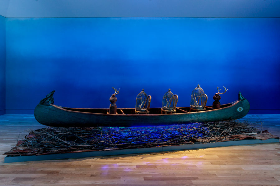 A wood canoe sits on top of a bed of dry branches in a blue room.