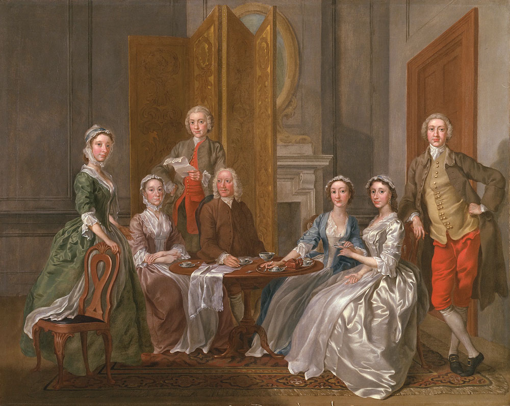 A family is gathered around a table with teatime service.