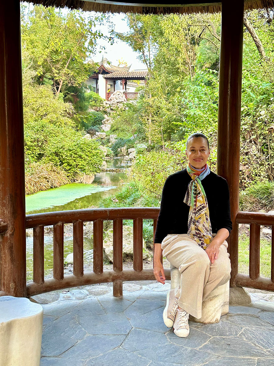 A person sits in a wooden pavilion with a stream in the background.