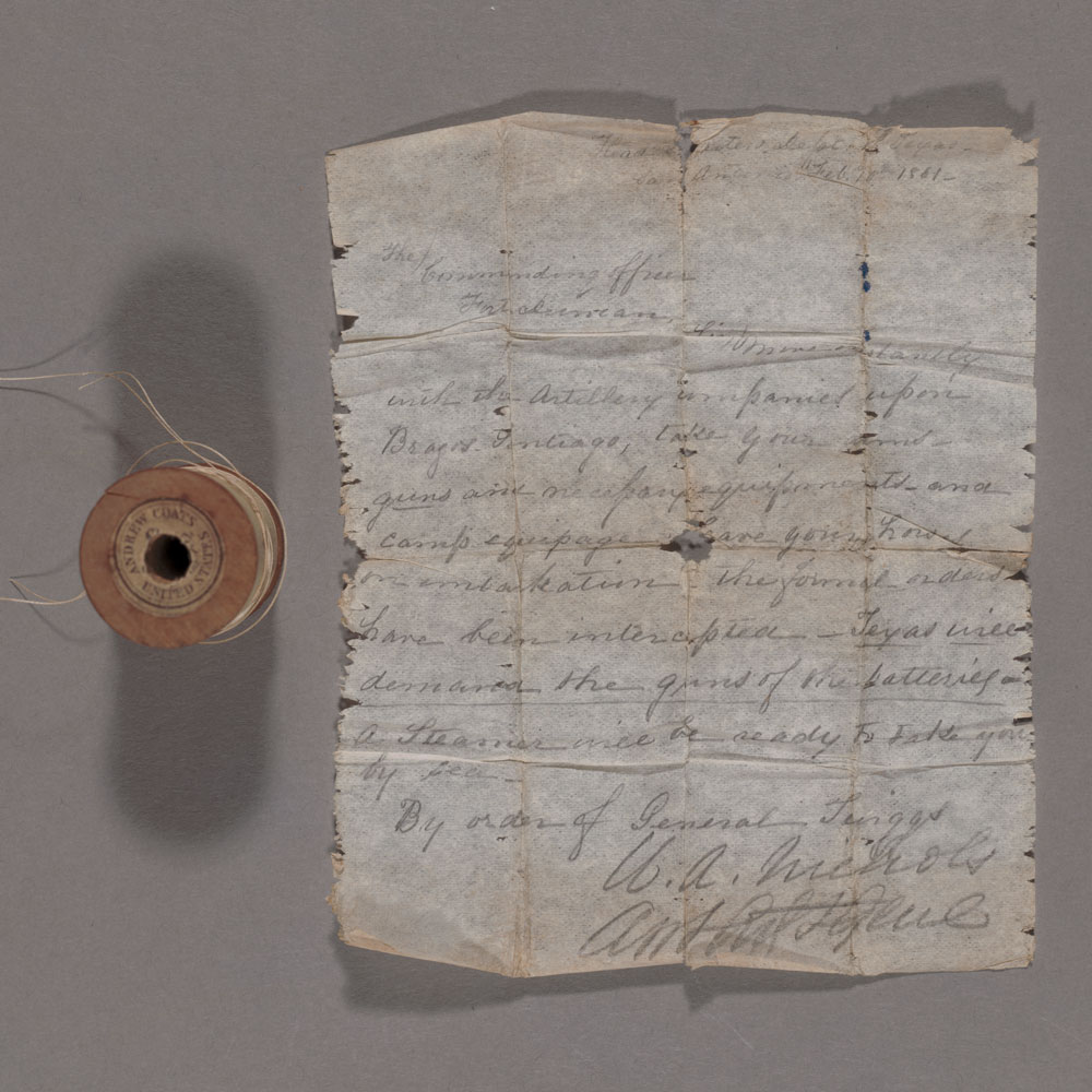 A spool of thread and a written note on folded paper.