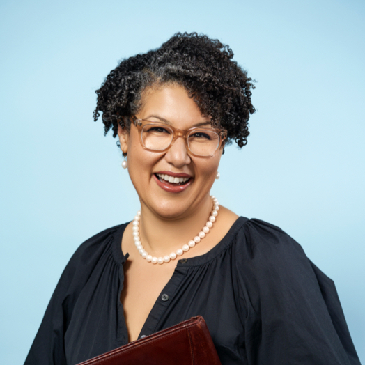 A smiling person with short curly hair and glasses.