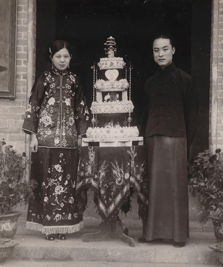 Black-and-white photo of two people standing on either side of a multitiered cake.