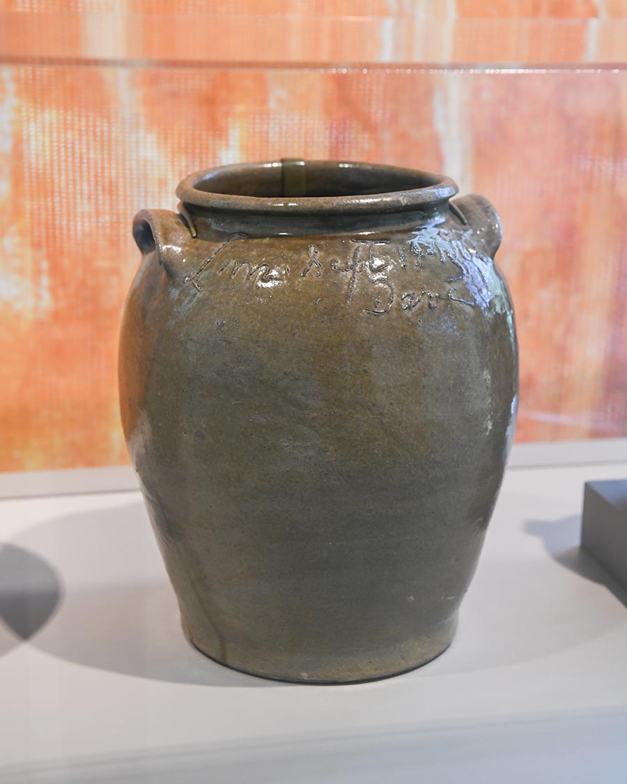 A large green-and-brown storage jar in a clear display box.