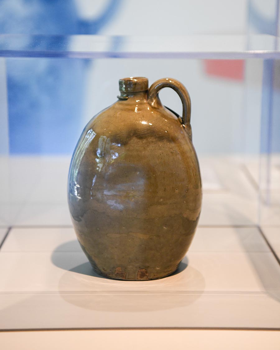 A brown glazed stoneware jug in a clear display box.