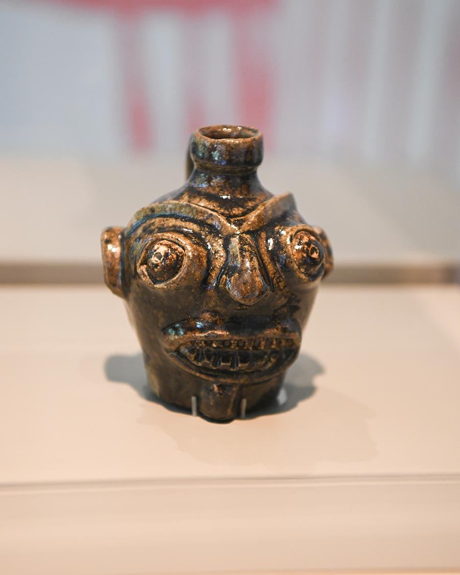A small green-and-brown jug with a carved face on a table.