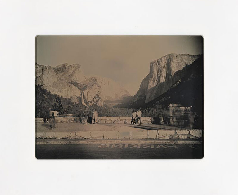 Black-and-white photograph of people at a lookout point of large mountains and a forested valley.