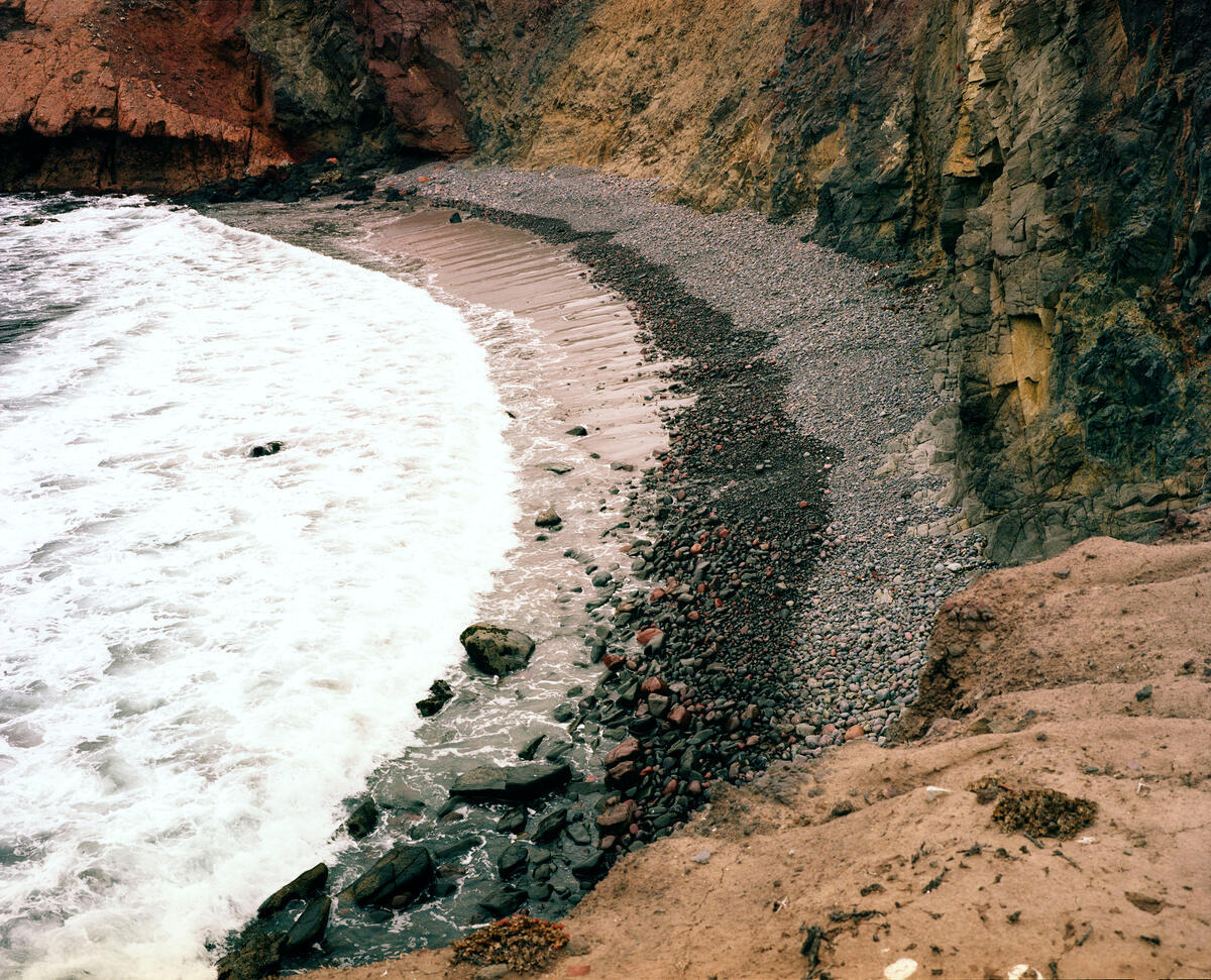 An overhead view of a beach, where segmented layers of sand and rocks are visible along the tide.