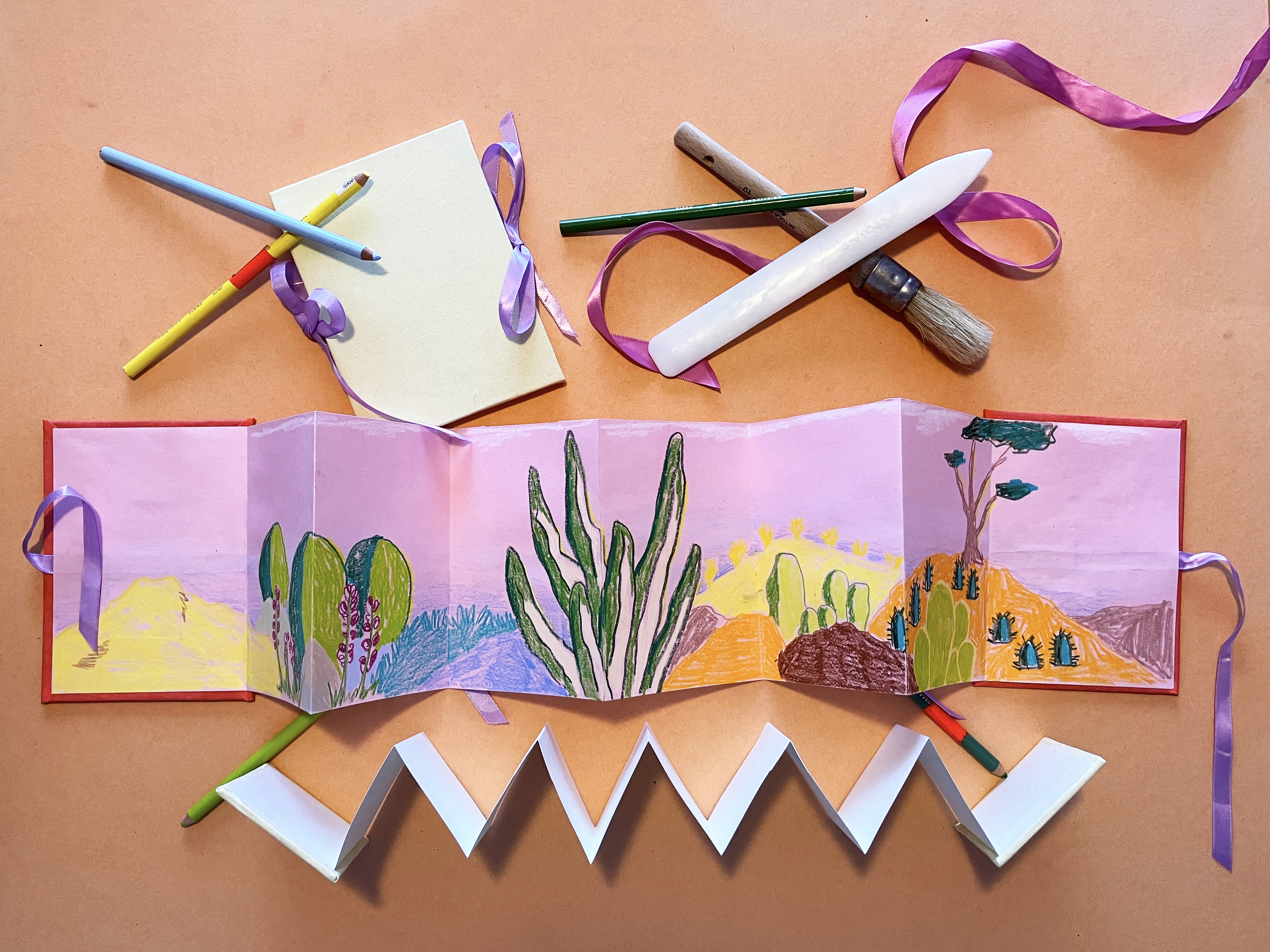 Overhead view of a table with an accordion style book and various crafting supplies.