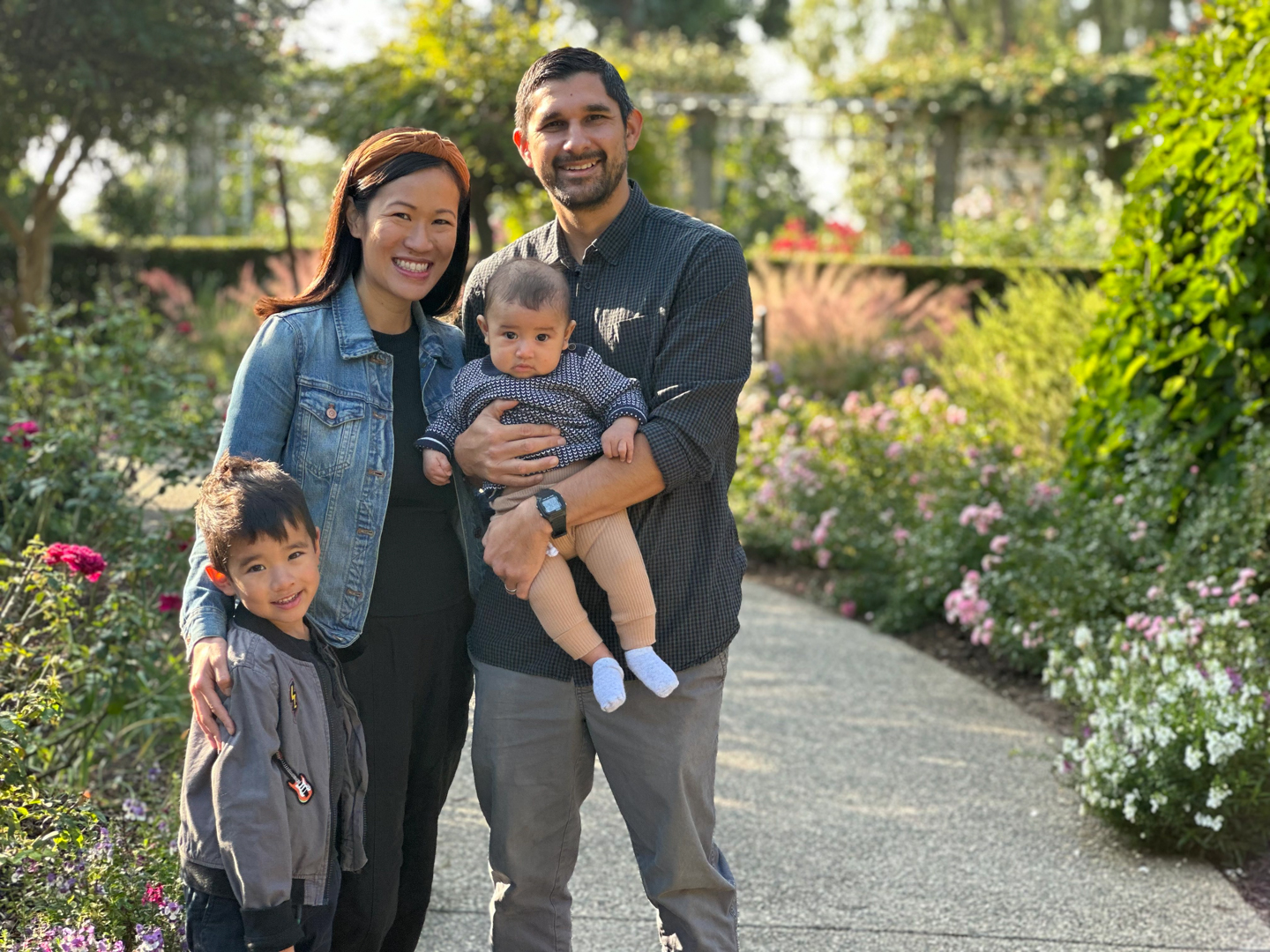 Two parents stand with their young children in a garden.