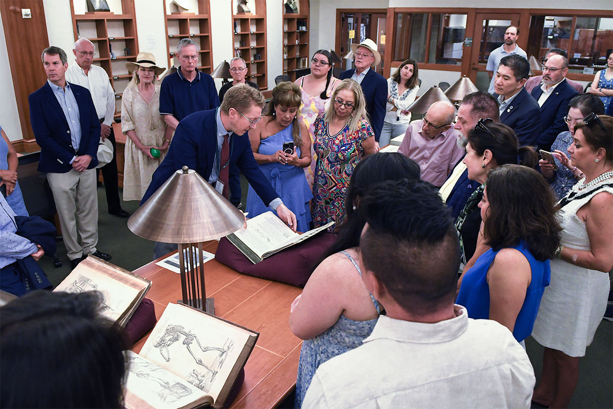 A crowded room in a library where several open books are on display.