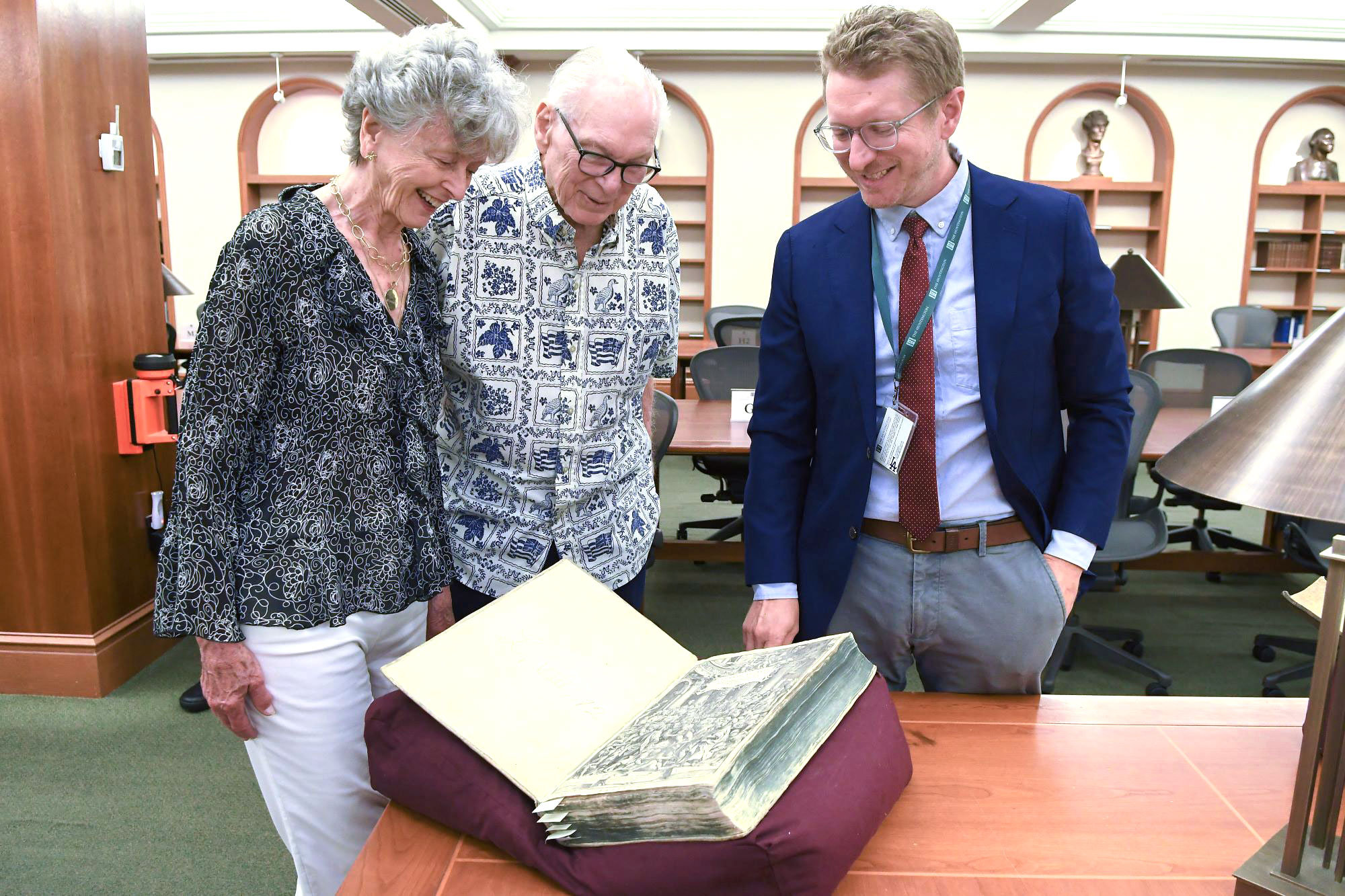 Three people look at an open book in a library.